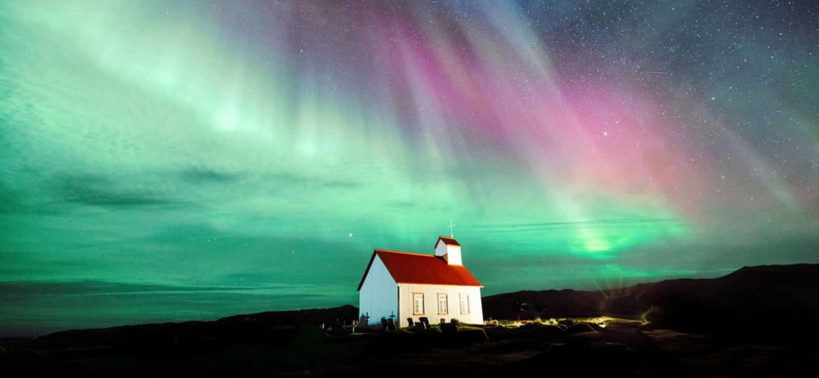 Chiesa isolata sotto un'aurora boreale colorata in cielo stellato.